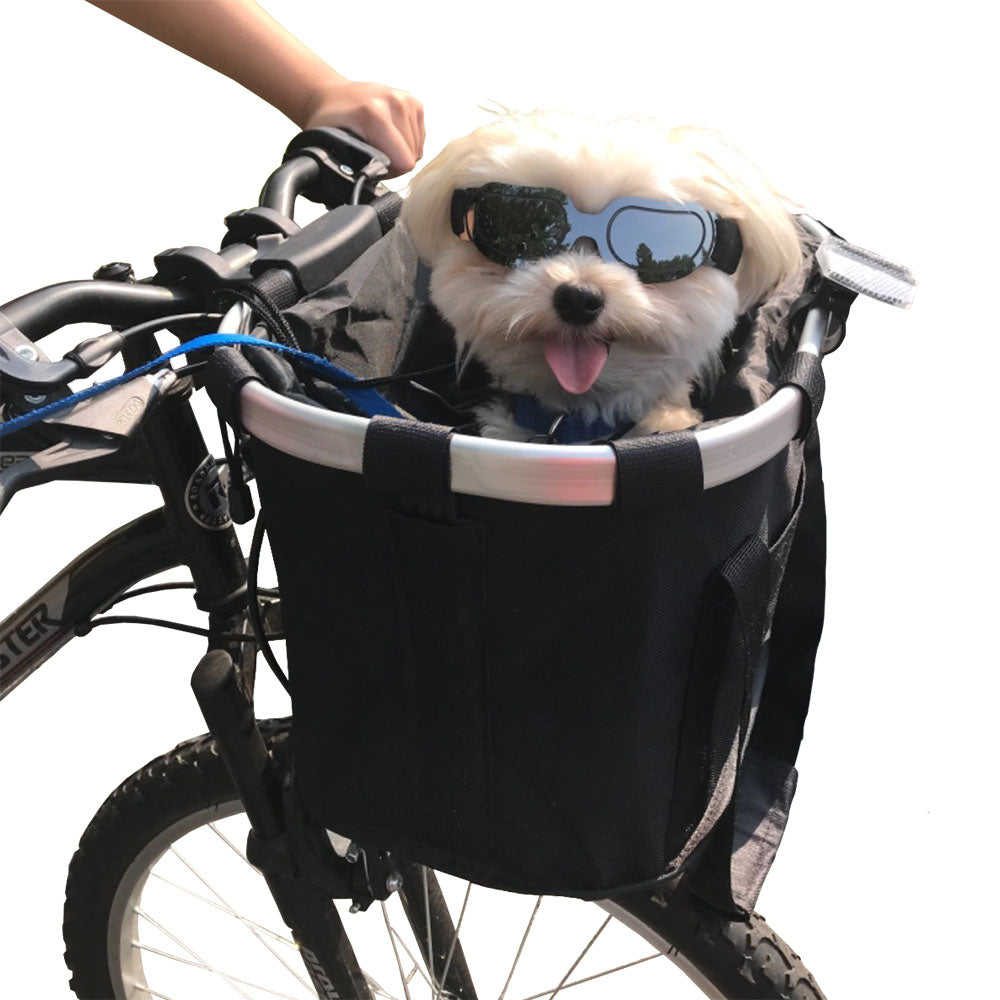 Small white dog with googles in a black Pawsket™ - Pet Bike Basket Carrier on a bike close up pictures on a white background.